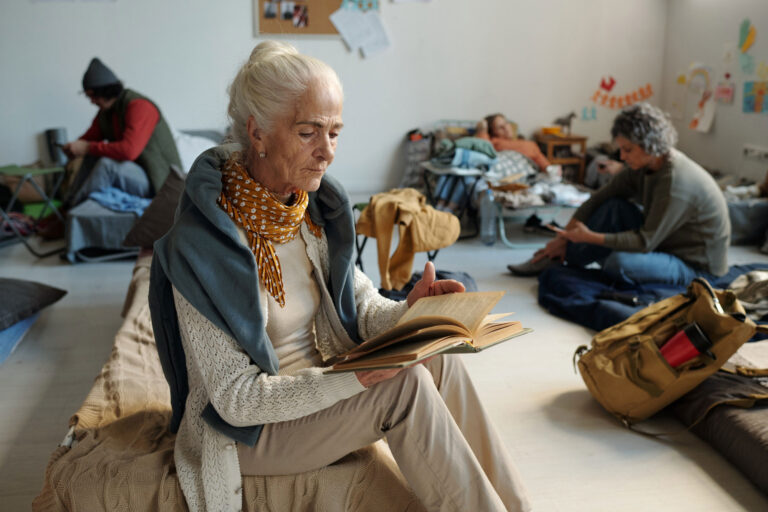 Elderly woman sitting on the ground reading a book, symbolizing lifelong learning and the power of personal stories