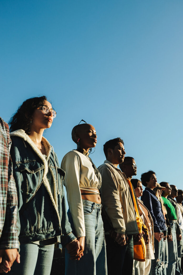 Group standing in a line holding hands, looking serious, symbolizing unity, resilience, and human rights solidarity