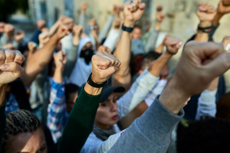 Group of people raising fists in the air to show solidarity and support for human rights, shared by Humanitas Media.