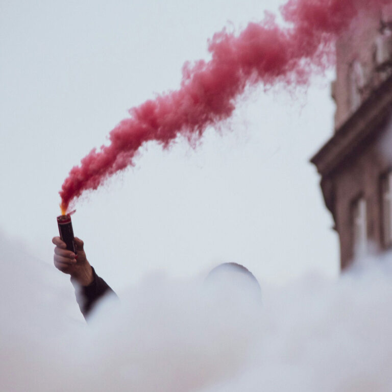 Hand holding a red flare symbolizing protest, urgency, and collective action for human rights